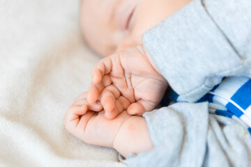 Newborn Baby Sleeping. Cute Infant Child in Wrap Bodysuit. New Born Little Boy smile in Blue Clothes lying on Blanket. Small Kid Face Close up Portrait holding Hands First