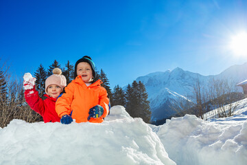 Fototapeta na wymiar Baby girl play snowball sitting in snow fortress over mountains