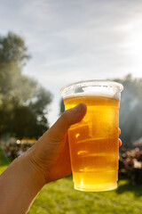 A plastic glass of beer in hand. Outdoor summer festival.
