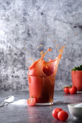 tomato juice, pour tomato juice into a glass, splashes of tomato juice, on a gray background, space for text, cherry tomatoes and salt 