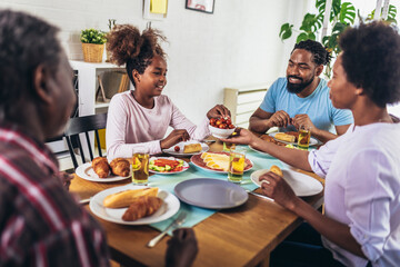 A multi-generational African-American family enjoying food at their dinner table.