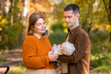A happy traditional family walks in the autumn park with a newborn baby on a sunny day.