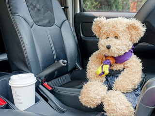 The scout bear sits in the driver's seat of the sedan with a cup of coffee next to it.    