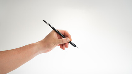 A man's hand holds a calligraphy and writing pen in his left hand on a white background.
