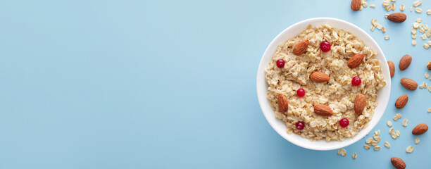 Bowl of tasty sweet oatmeal with nuts on light blue background with space for text, top view
