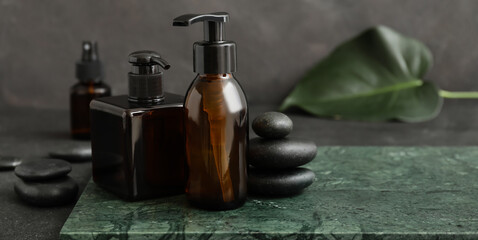 Obraz na płótnie Canvas Bottles of natural shampoo and spa stones on dark background