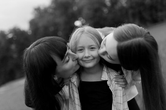 A mother and two daughters are playing on the street. Mother and older daughter kiss the younger one. Spend time together. Happy family concept. Black and white photo
