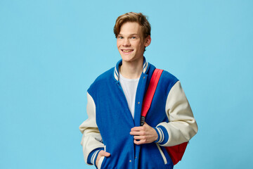 a handsome young student stands with a backpack on his back and holds the edges of his jacket with...