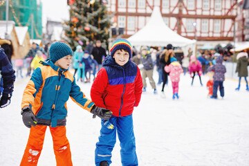 Two happy kids boys in colorful warm clothes skating on a rink of Christmas market or fair. Healthy...
