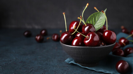 Bowl of tasty cherries on dark background with space for text