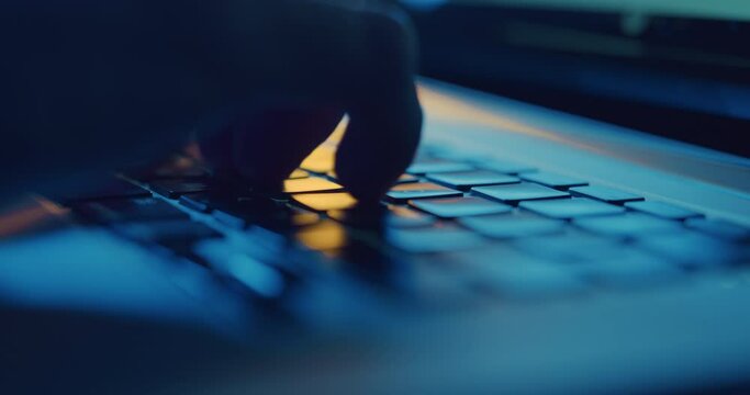 Close up of hands typing on laptop keyboard at night