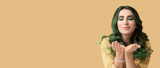 Beautiful young woman with unusual green hair blowing kiss on beige background with space for text