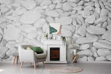 Interior of light living room with fireplace, armchair and wall with print of stones