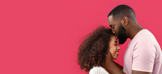 Young African-American man kissing his girlfriend on red background with space for text