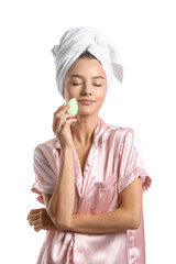 Pretty young woman with green makeup sponge on white background