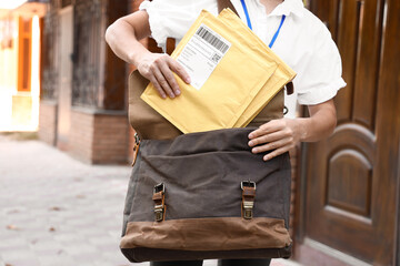 Young postwoman with letters and bag outdoors