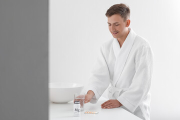 Young man with glass of water and pills in bathroom