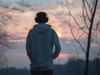 A young man listens to music with headphones while walking in the park at an autumn sunset .