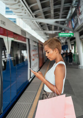 Side View Of Beautiful Woman Holding Shopping Bags And Using Mobile Phone While Standing At Railway Platform