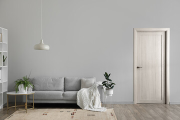 Grey sofa and table with houseplants near light wall