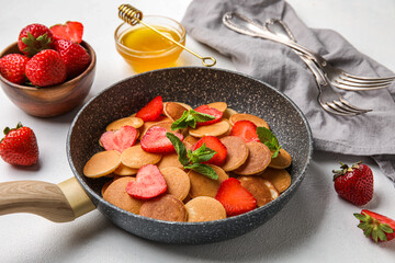 Frying pan with mini pancakes and strawberry on light table