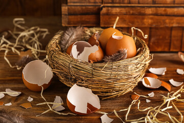 Nest with broken egg shells and feathers on wooden table
