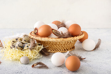 Bowl and nest with different eggs and feathers on light background