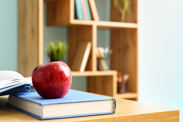 Red apple with school books on desk in classroom, closeup