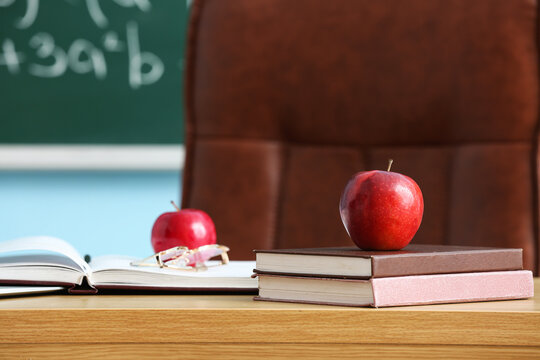 Red apple with school books on desk in classroom, closeup