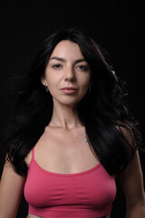 Fototapeta premium A smiling young woman model in a pink tank top in the studio. Posing on a black background. Portrait