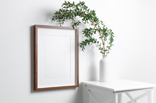 Blank vertical frame mockup for artwork or picture on white wall with eucalyptus twigs.