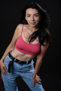 Smiling young woman model in pink tank top and jeans in studio. Set on a black background.