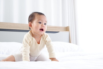 Fototapeta premium A cute little boy is sitting on a white mattress with a happy smile.
