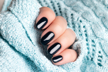 Female hand in blue knitted sweater with beautiful manicure - dark black nails. Nail care concept
