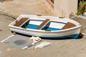 Small white and blue rowing boat moored on the quay of the port, a beach towel, sun hat and...