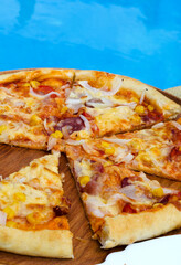 Pizza cut into slices on the background of a blue pool.