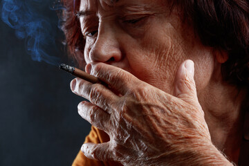 Close up of old woman smoking a cigarette. Cigarette in an elderly wrinkled female hand. Concepts...