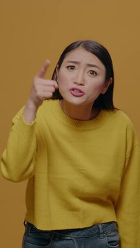 Vertical video: Angry woman showing index finger at camera and having argument, feeling furious and insulted in studio. Offended person arguing and having negative reaction, annoyed facial expression.