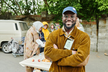 Portrait of African volunteer standing outdoors with his arms crossed and smiling at camera, he...