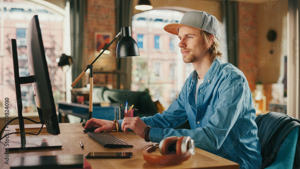 Poster young handsome man working from loft apartment on desktop computer. creative male checking social me