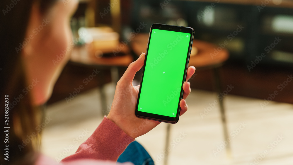 Poster feminine hand holding a smartphone with green screen mock up display. female is resting at home, wat