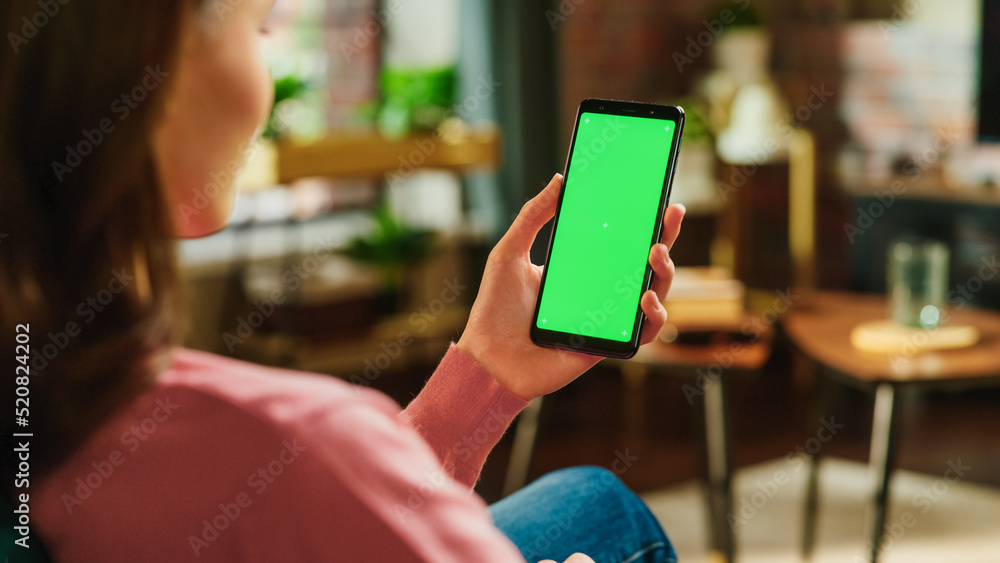 Poster Feminine Hand Tapping on Display and Scrolling Feed on Smartphone with Green Screen Mock Up Display. Female Resting at Home, Checking Social Media on Mobile Device. Close Up Over the Shoulder Photo.