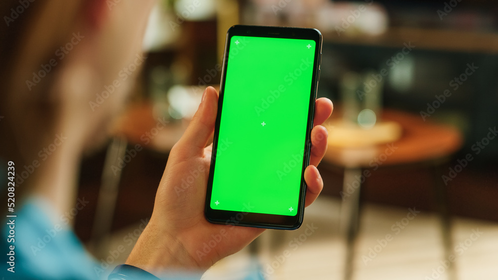 Poster Man Swiping on Display and Scrolling Feed on Smartphone with Green Screen Mock Up Display. Male Resting at Home, Checking Social Media on Mobile Device. Close Up Over the Shoulder Photo.
