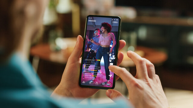Man Scrolling Feed of Social Media Application and Double Tapping on Display on Smartphone. Male Resting at Home, Checking Social Network on Mobile Device. Close Up Over the Shoulder Photo.