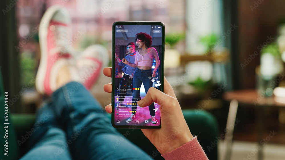 Leinwandbilder feminine hand scrolling social media feed on smartphone display. female is relaxing on sofa at home,