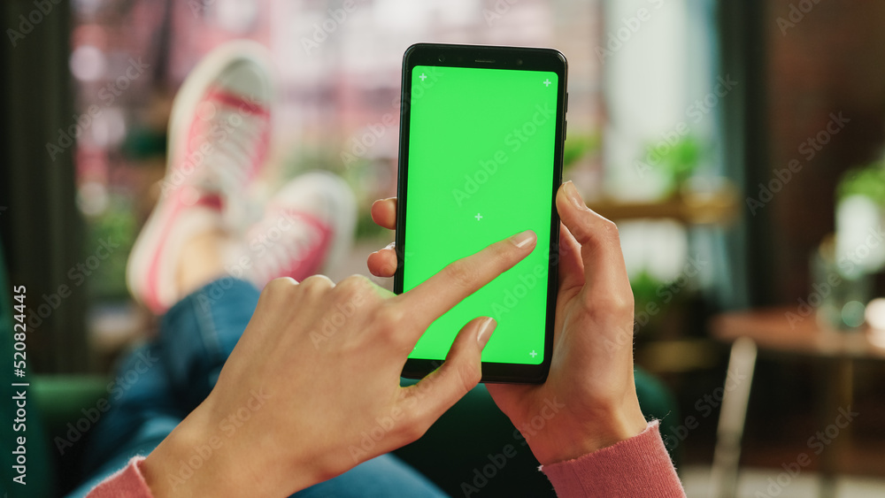 Leinwandbilder feminine hand scrolling feed on smartphone with green screen mock up display. female is relaxing on 