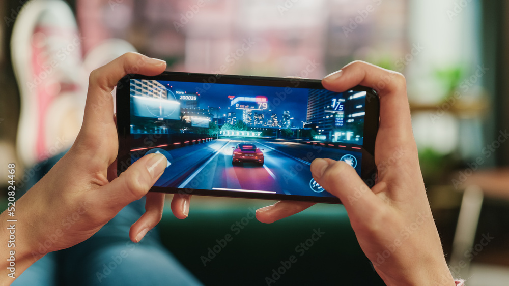 Poster female is relaxing on a couch at home, playing an interactive racing drift video game on her smartph