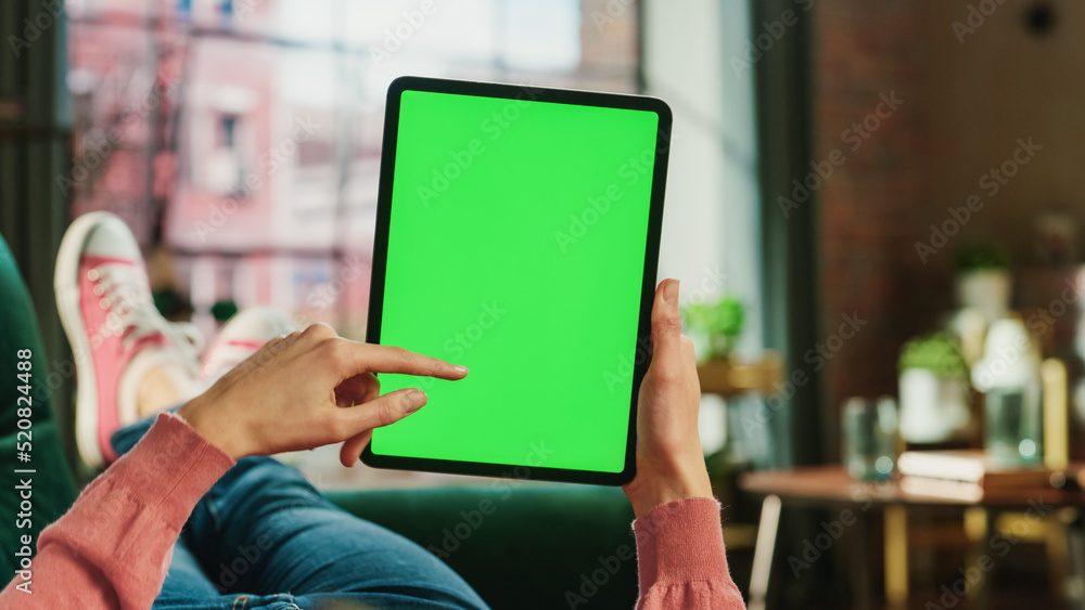 Poster feminine hand scrolling feed on tablet with green screen mock up display. female is relaxing on sofa
