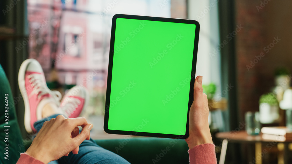 Poster feminine hand scrolling feed on tablet with green screen mock up display. female is relaxing on sofa