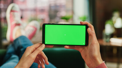 Woman Horizontally Holding a Smartphone with Green Screen Mock Up Display. Female is Relaxing on a...